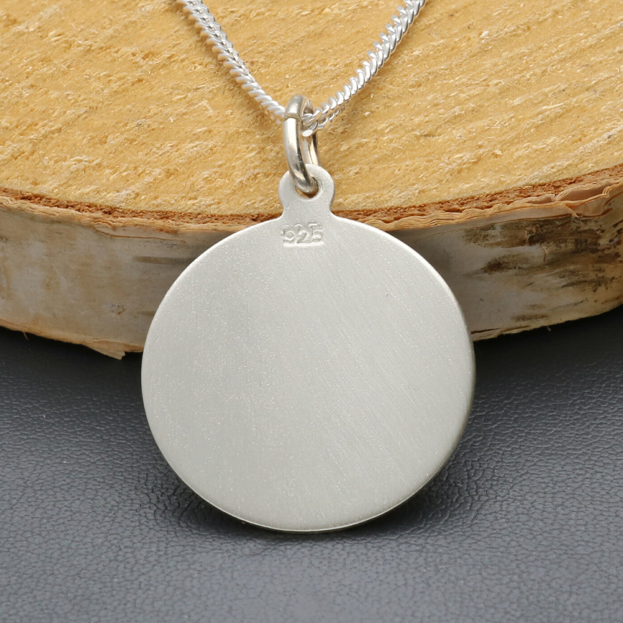 Silver pendant necklace on a wooden block with a gray surface
